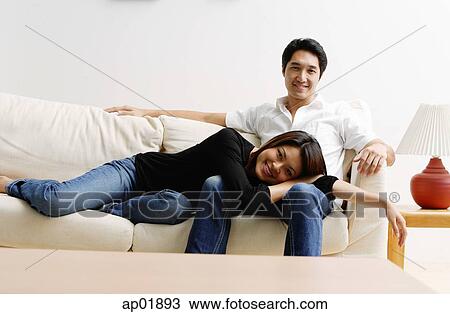 Stock Image - Couple on sofa, woman lying on mans lap, looking at camera. Fotosearch