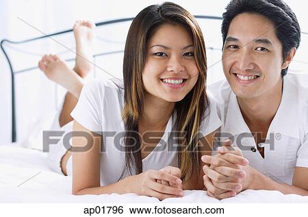 Couple side by side on bed, smiling at camera View Large Photo Image Stock Photograph - Couple side by side on bed, smiling at camera. Fotosearch