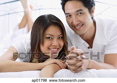 Stock Photo - Couple side by side on bed, smiling. Fotosearch