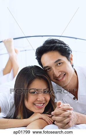 Stock Photo - Couple side by side on bed, smiling, portrait. Fotosearch