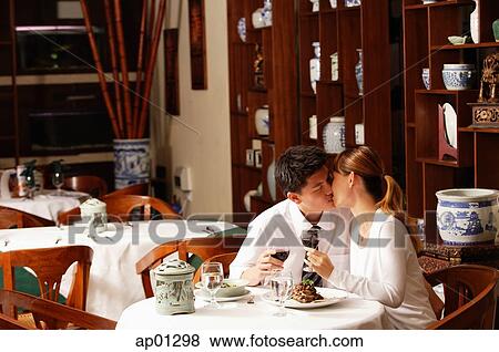 Stock Photo - Couple sitting in restaurant, kissing. Fotosearch