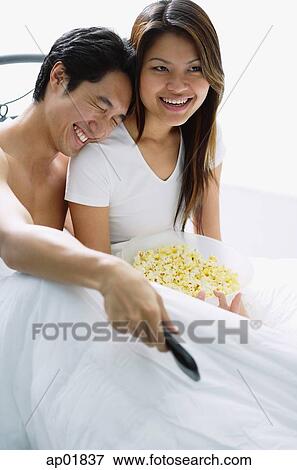 Couple sitting on bed, smiling, watching TV, man leaning on womans shoulder View Large Photo Image Stock Photo - Couple sitting on bed, smiling, watching TV, man leaning on womans shoulder. Fotosearch