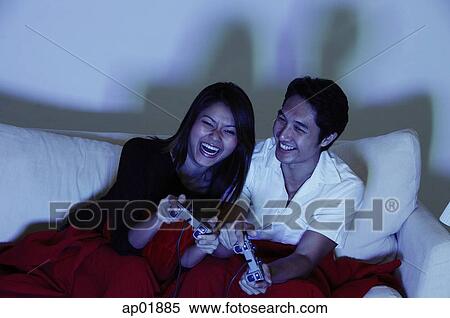 Couple sitting on sofa, playing with video games View Large Photo Image Stock Photography - Couple sitting on sofa, playing with video games. Fotosearch