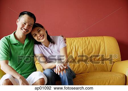 Couple sitting on sofa, side by side, looking at camera View Large Photo Image Stock Image - Couple sitting on sofa, side by side, looking at camera. Fotosearch