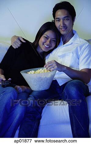 Stock Photo - Couple sitting on sofa, watching TV, portrait. Fotosearch