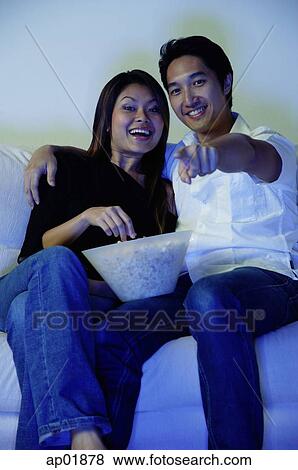 Couple sitting on sofa, watching TV, man pointing finger View Large Photo Image Stock Photo - Couple sitting on sofa, watching TV, man pointing finger. Fotosearch