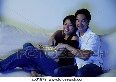 Couple sitting on sofa, watching TV, eating popcorn View Large Photo Image Stock Photo - Couple sitting on sofa, watching TV, eating popcorn. Fotosearch