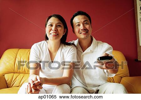 Couple sitting on sofa, watching TV, man holding TV remote control View Large Photo Image Stock Photography - Couple sitting on sofa, watching TV, man holding TV remote control. Fotosearch