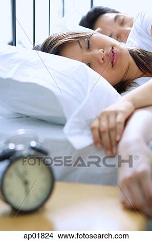 Couple sleeping on bed, alarm clock in foreground, selective focus View Large Photo Image Picture - Couple sleeping on bed, alarm clock in foreground, selective focus. Fotosearch