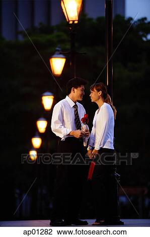 Couple standing face to face, man holding single rose stalk View Large Photo Image Stock Image - Couple standing face to face, man holding single rose stalk. Fotosearch