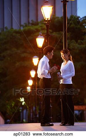 Stock Image - Couple standing face to face, under streetlights. Fotosearch