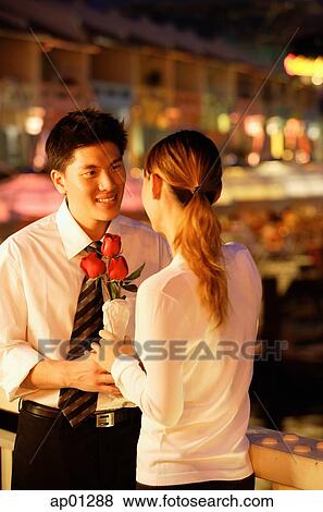 Couple standing face to face, woman holding roses View Large Photo Image Stock Photo - Couple standing face to face, woman holding roses. Fotosearch