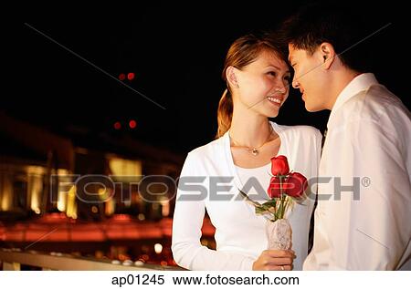 Couple standing face to face, woman holding single rose stalk, portrait View Large Photo Image Stock Photography - Couple standing face to face, woman holding single rose stalk, portrait. Fotosearch
