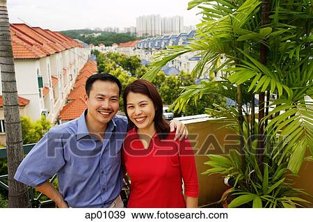 Stock Photo - Couple standing on balcony, smiling at camera. Fotosearch