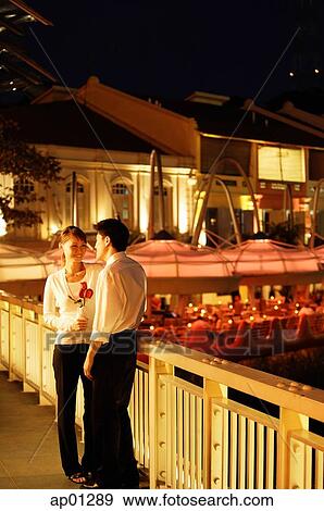 Couple standing on bridge, woman holding roses View Large Photo Image Stock Photo - Couple standing on bridge, woman holding roses. Fotosearch