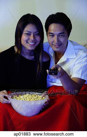 Couple watching TV, woman holding bowl of popcorn, man holding remote control View Large Photo Image Stock Image - Couple watching TV, woman holding bowl of popcorn, man holding remote control. Fotosearch