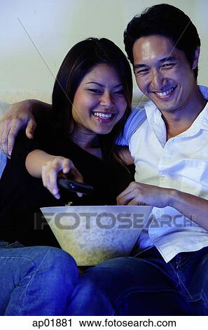 Stock Image - Couple watching TV, woman holding remote control. Fotosearch