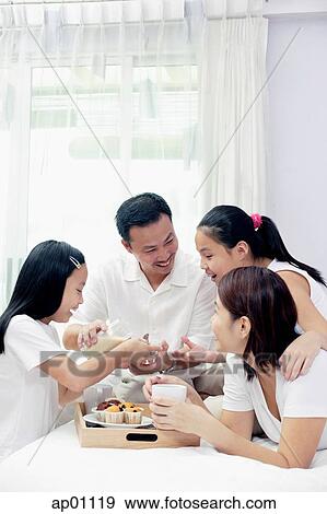 Stock Photo - Family of four in bedroom, having breakfast in bed. Fotosearch