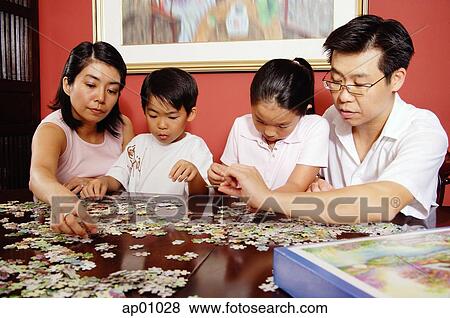 Stock Photo - Family of four, jigsaw puzzle pieces spread around them. Fotosearch