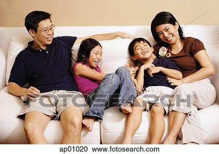 Stock Image - Family of four on sofa, laughing. Fotosearch