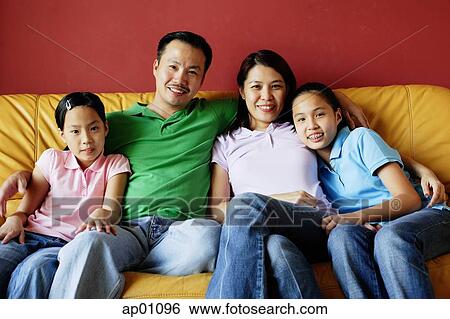 Stock Photograph - Family of four sitting on sofa, looking at camera. Fotosearch