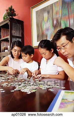 Stock Photograph - Family of four sorting jigsaw puzzle on table. Fotosearch