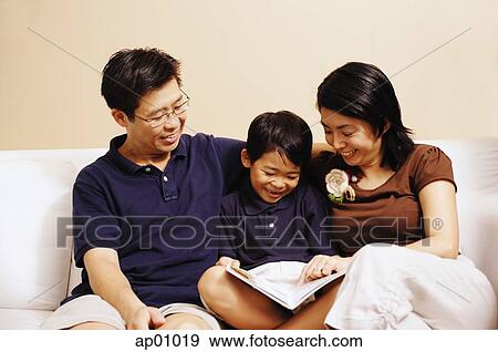 Stock Photo - Family with one son, sitting on sofa, looking at book. Fotosearch