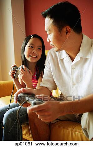 Stock Image - Father and daughter looking at each other, holding video game controllers. Fotosearch