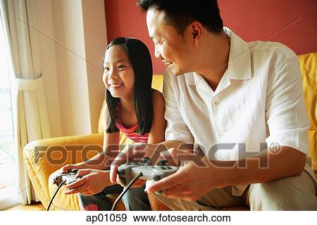 Stock Photo - Father and daughter sitting side by side playing video games. Fotosearch