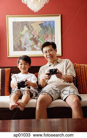 Stock Image - Father and son in living room, playing video game. Fotosearch