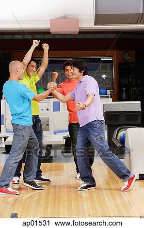 Stock Image - Four guys at a bowling alley, arms raised in victory. Fotosearch