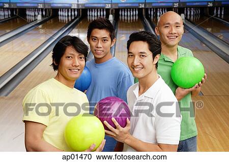 Stock Image - Four men in bowling alley, holding bowling balls. Fotosearch