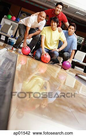 Stock Image - Four men in bowling alley, looking at camera. Fotosearch