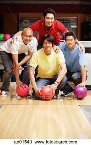 Stock Image - Four men in bowling alley, looking at camera, portrait. Fotosearch