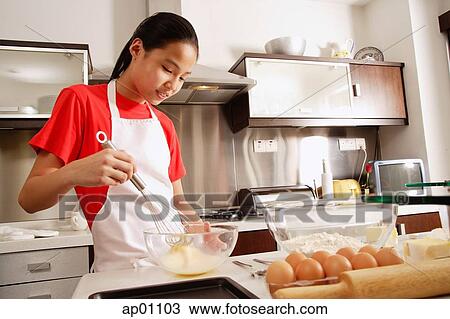 Stock Image - Girl in kitchen, holding whisk and bowl. Fotosearch