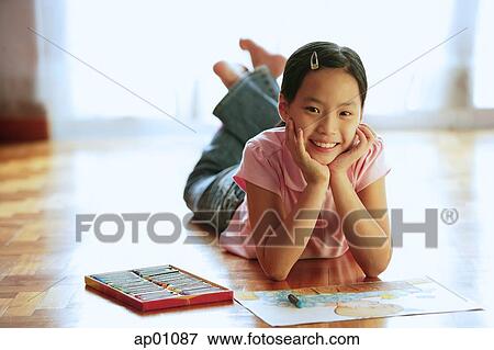 Stock Photo - Girl lying on floor, with paper and crayons, looking at camera, portrait. Fotosearch