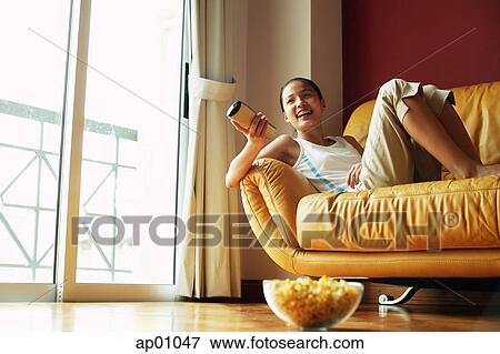 Stock Photo - Girl lying on sofa, holding remote control. Fotosearch
