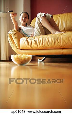 Girl lying on sofa, holding remote control, bowl of popcorn on the floor View Large Photo Image Stock Photo - Girl lying on sofa, holding remote control, bowl of popcorn on the floor. Fotosearch