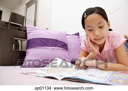 Picture - Girl reading magazine, lying on front, hand on chin. Fotosearch