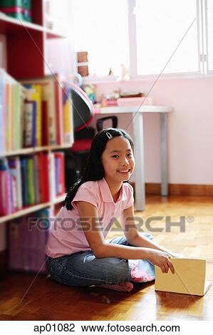 Girl sitting cross-legged on floor, holding book, looking at camera View Large Photo Image Stock Image - Girl sitting cross-legged on floor, holding book, looking at camera. Fotosearch