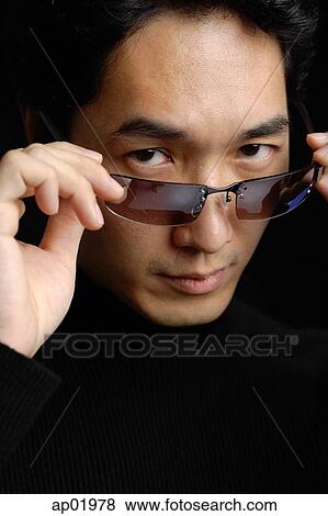 Stock Photo - Man adjusting sunglasses, looking at camera. Fotosearch
