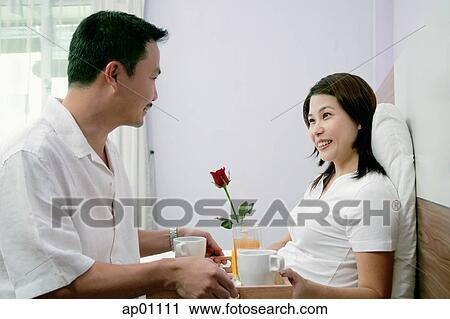 Stock Image - Man bringing woman breakfast in bed. Fotosearch
