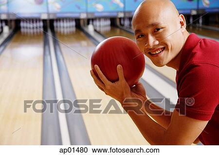 Stock Image - Man holding bowling ball, smiling at camera. Fotosearch