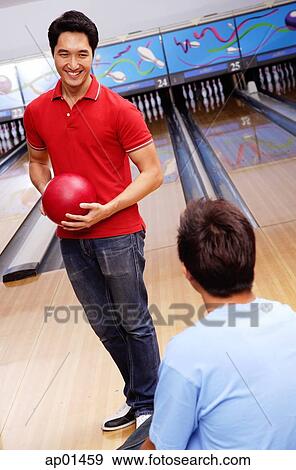 Stock Photo - Man holding bowling ball, standing in bowling alley. Fotosearch
