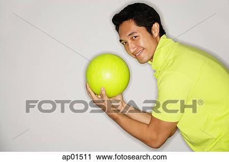 Stock Image - Man holding bowling ball, turning to smile at camera. Fotosearch