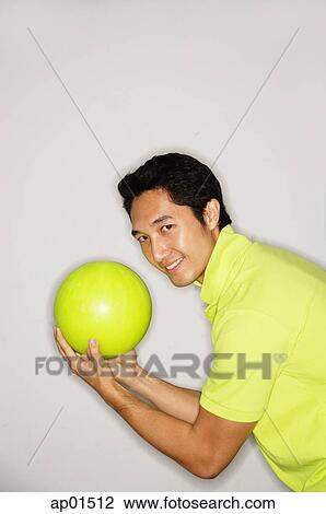 Stock Image - Man holding bowling ball, turning to look at camera. Fotosearch