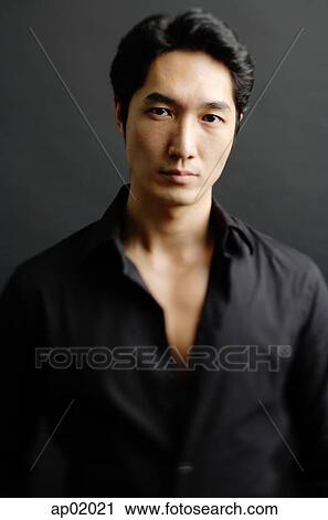 Stock Image - Man in black shirt, standing against black background. Fotosearch