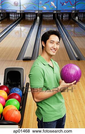 Stock Photo - Man in bowling alley, holding bowling ball, looking at camera. Fotosearch