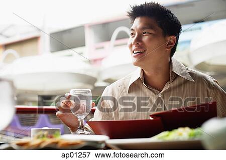 Stock Photo - Man in cafe, menu in front of him, holding glass of water, looking away. Fotosearch