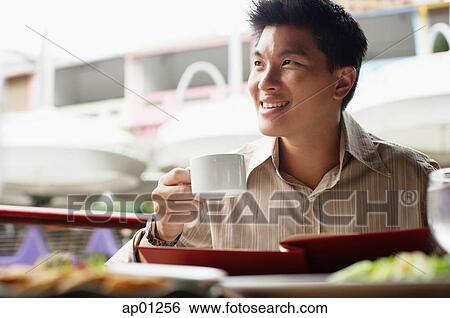 Stock Photograph - Man in cafe, menu in front of him, holding cup, looking away. Fotosearch